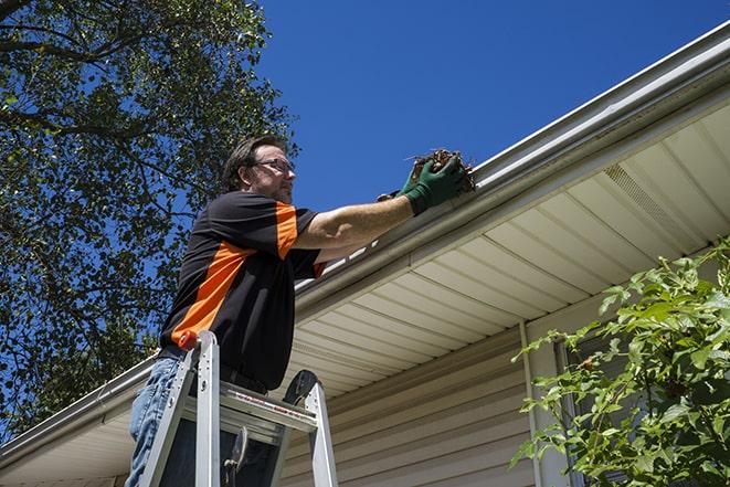 maintenance worker using a ladder to repair a gutter in Ault